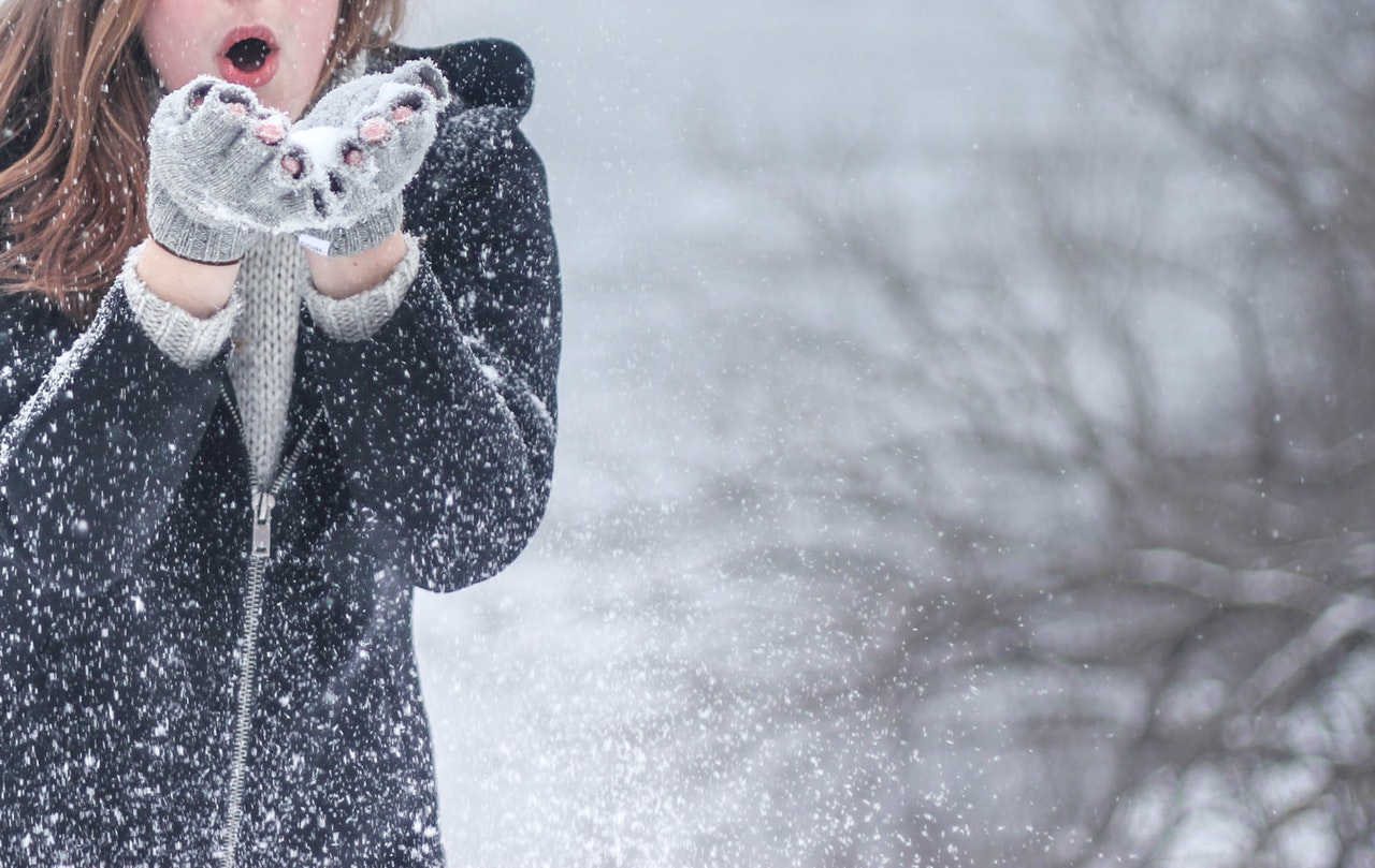 Young woman blowing snow toward camera on winter background