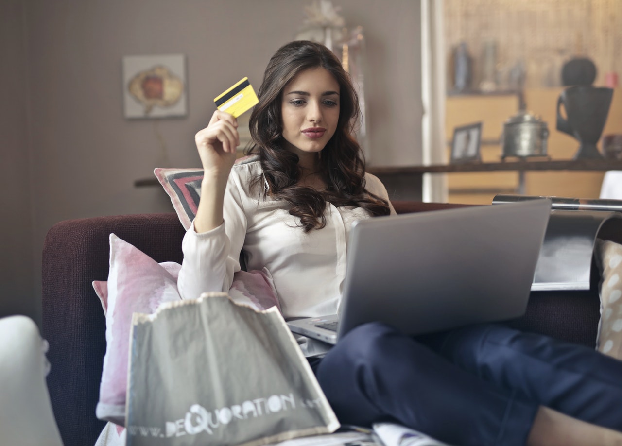 Brunette sitting with laptop in her lap holding credit card